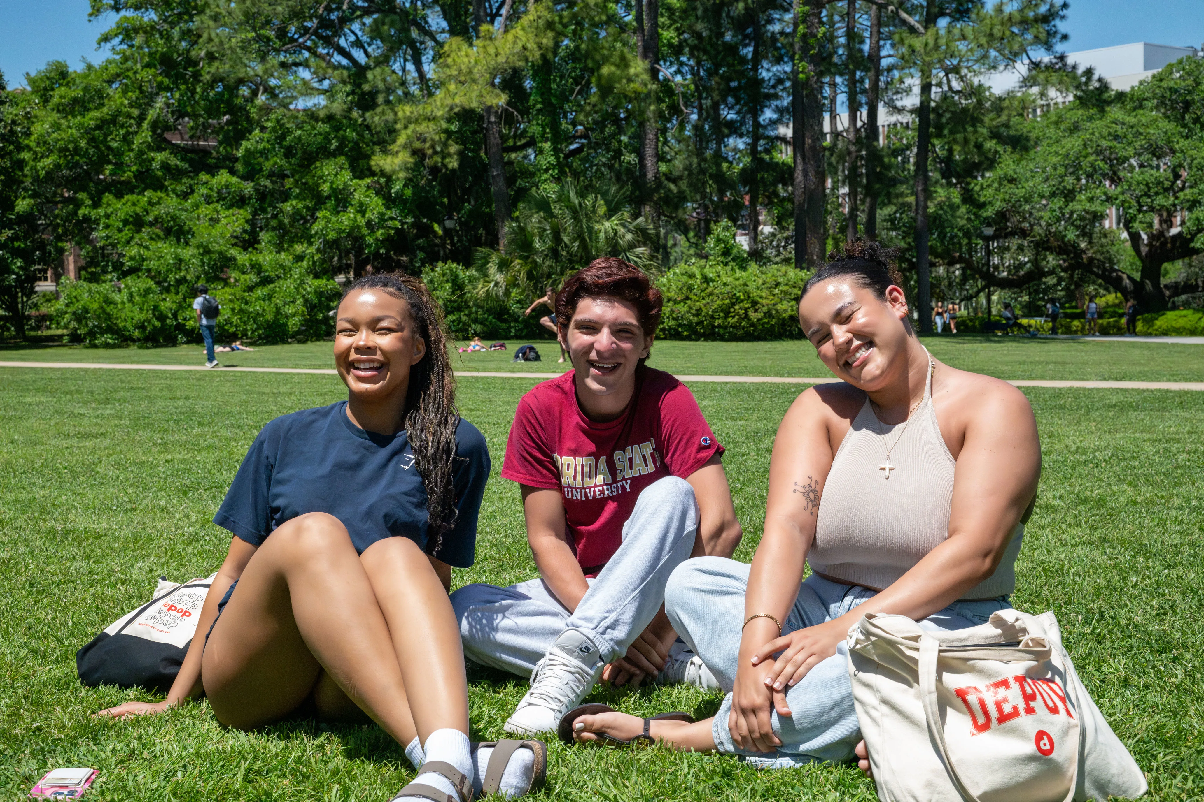 Three students sitting and smiling on the grass